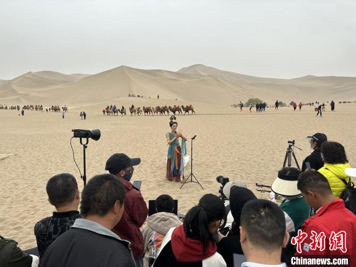 圖為2023年4月底，敦煌大漠“逐舞者”奧楠在鳴沙山月牙泉景區(qū)視頻直播，吸引游人圍觀。　馮志軍 攝