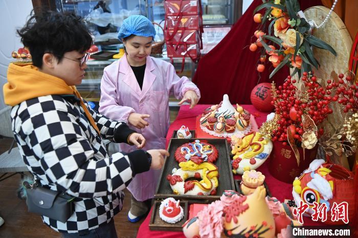 1月25日，隨著春節(jié)臨近，蘭州一花饃店“龍”元素花饃熱銷。圖為工作人員向顧客推薦“龍”元素花饃。九美旦增 攝</p><p>